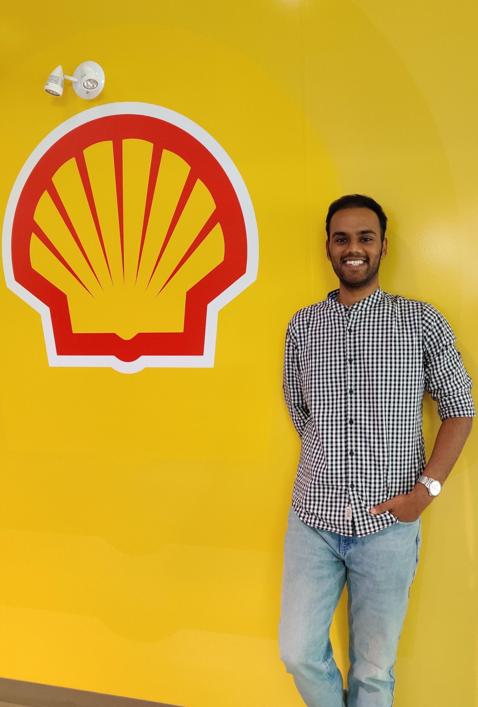 Narayanan (Nana) Ramakrishnan standing in front of a yellow wall, with a Shell Canada logo smiling.