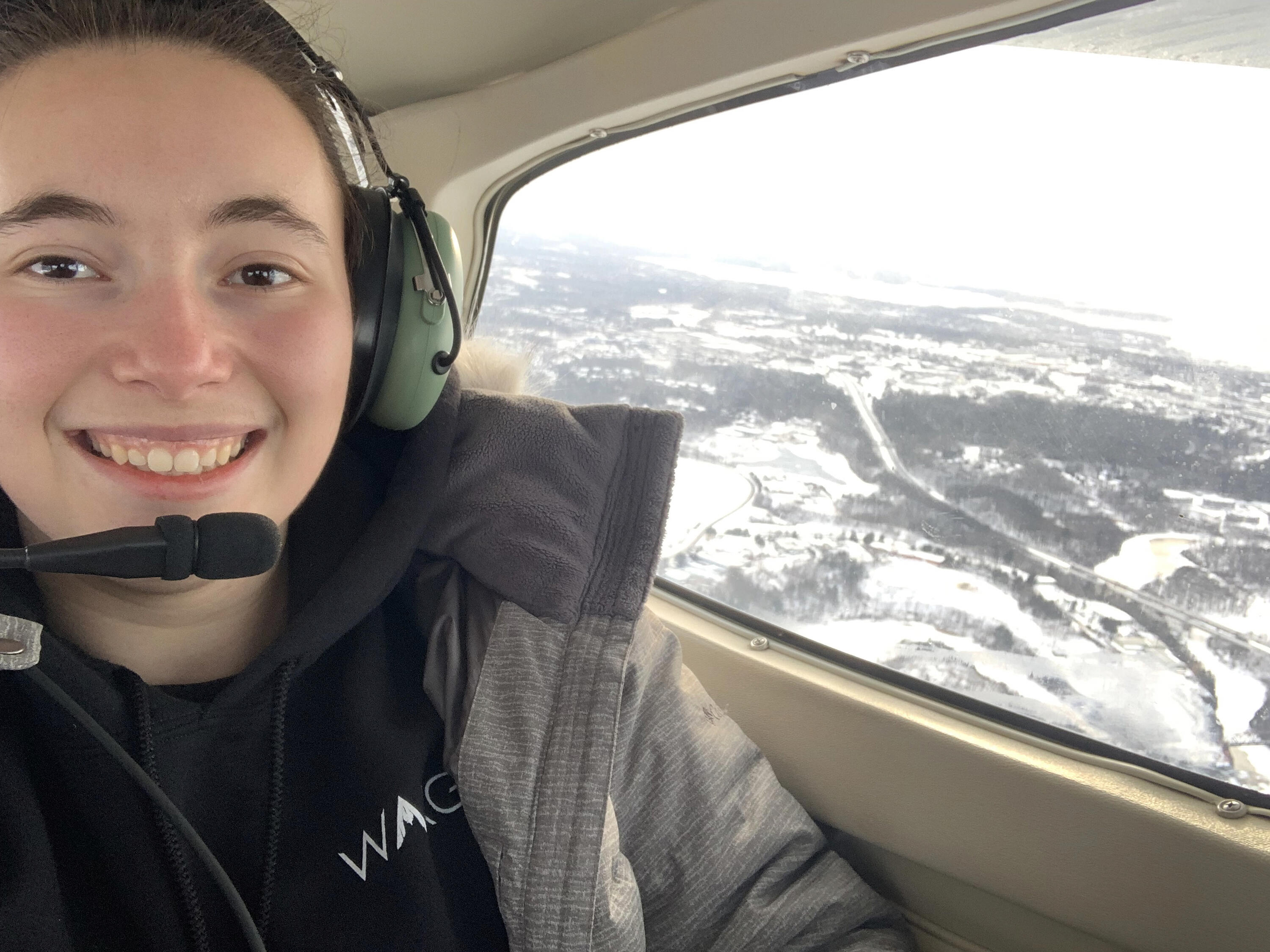 Brielle in a small airborne plan. Smiling with a headset on.