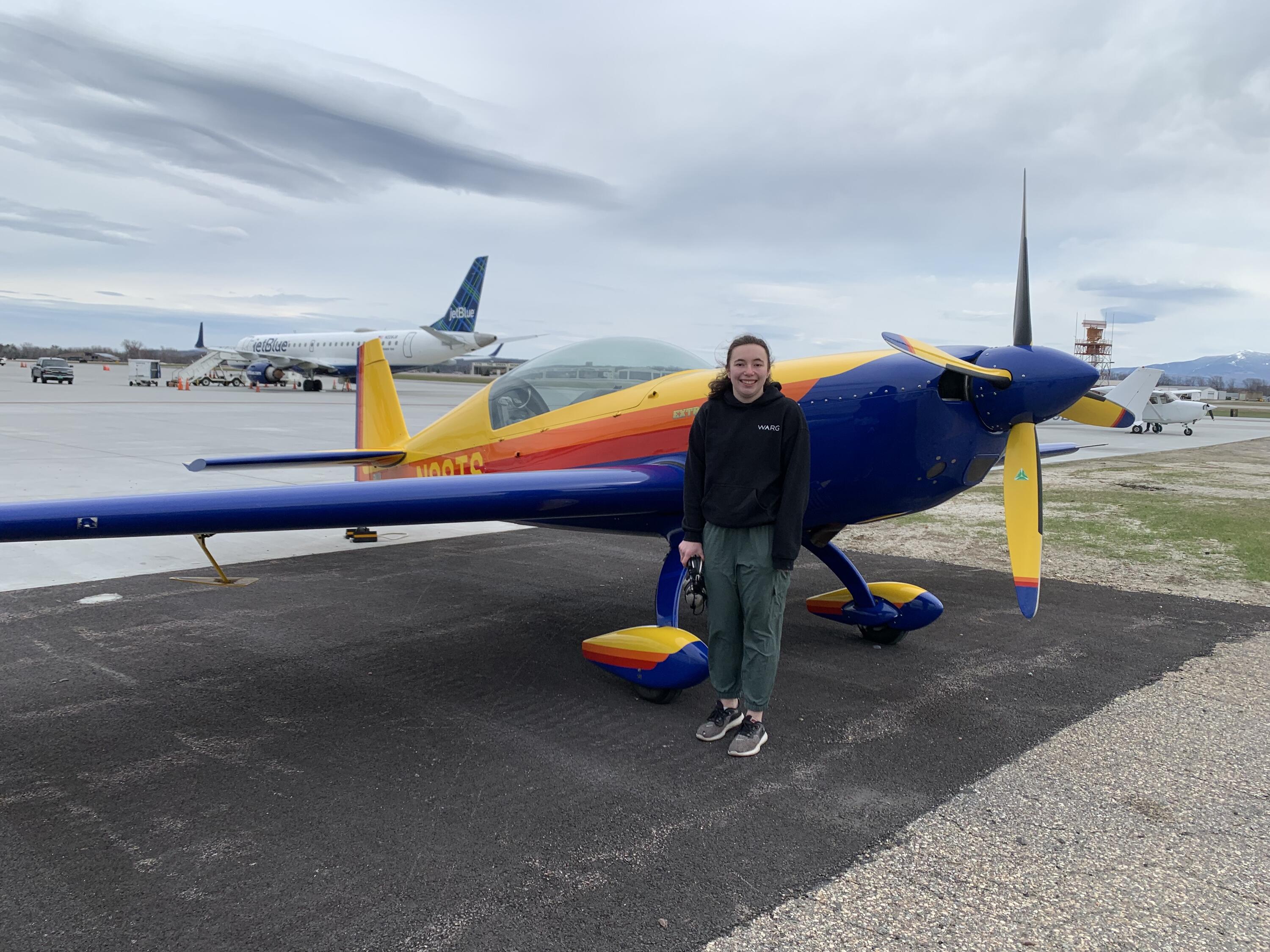 Brielle standing in front of a small, grounded, colourful plane
