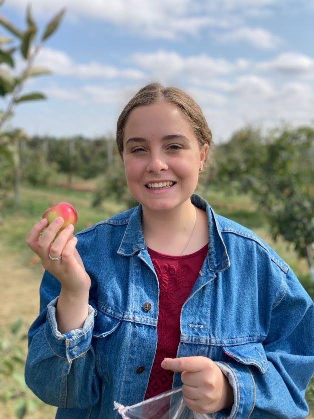Photo of Daynica smiling outside while holding an apple in her hand 