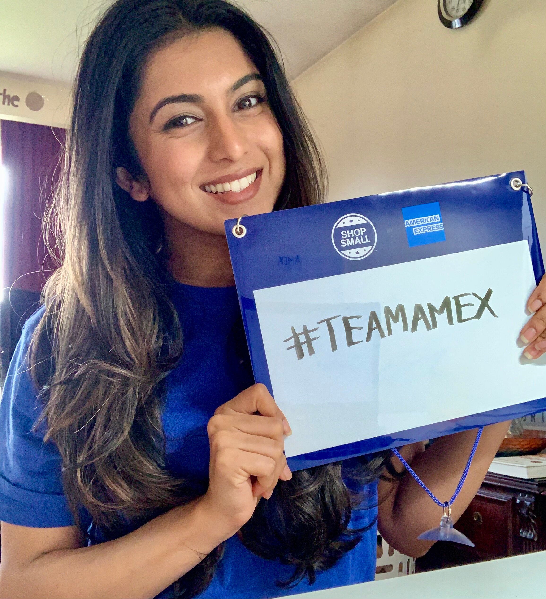A photo of Rashmi smiling while holding a board that says #TEAMAMEX
