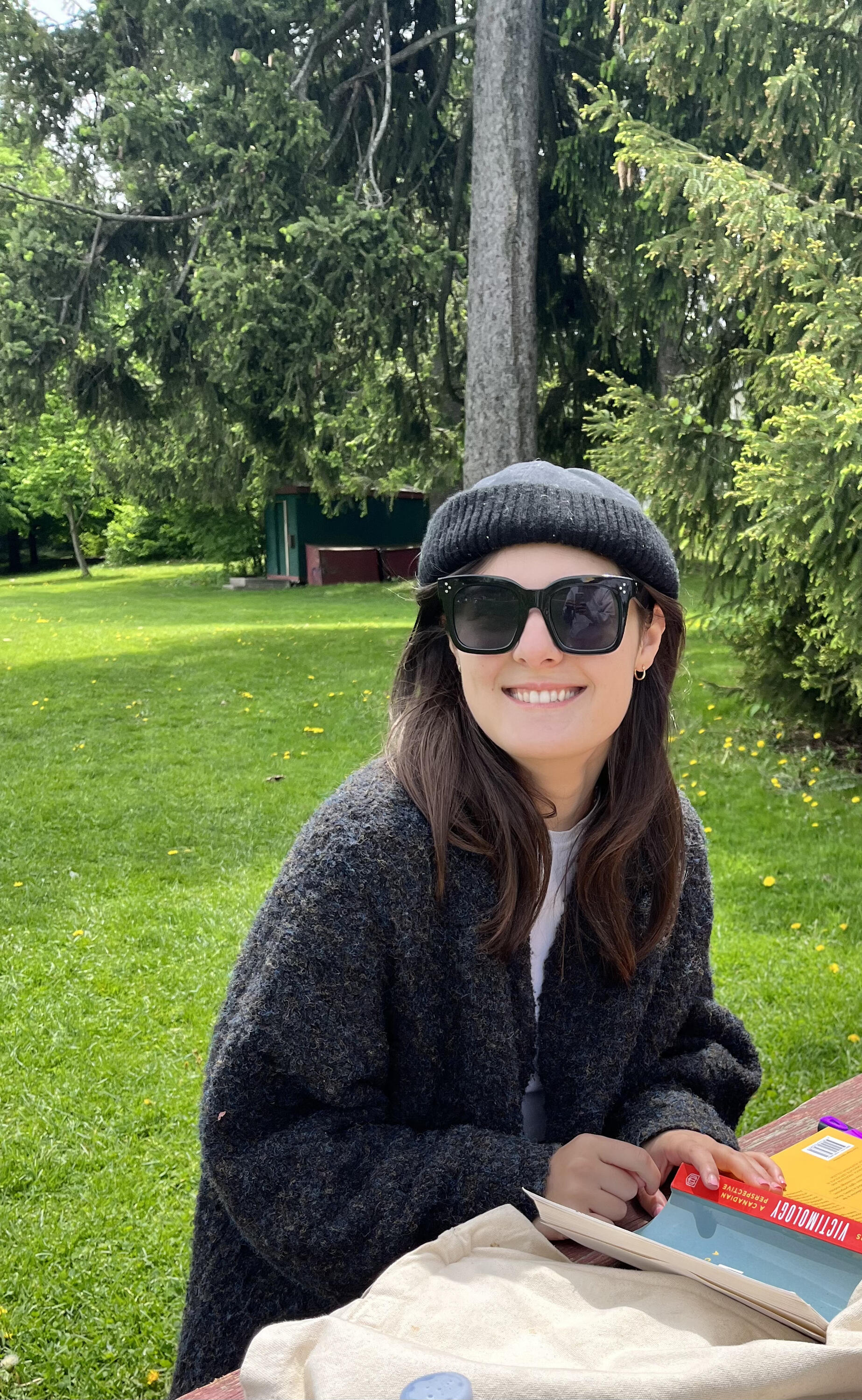A photo of Sydney sitting at a table in a park, wearing sunglasses.