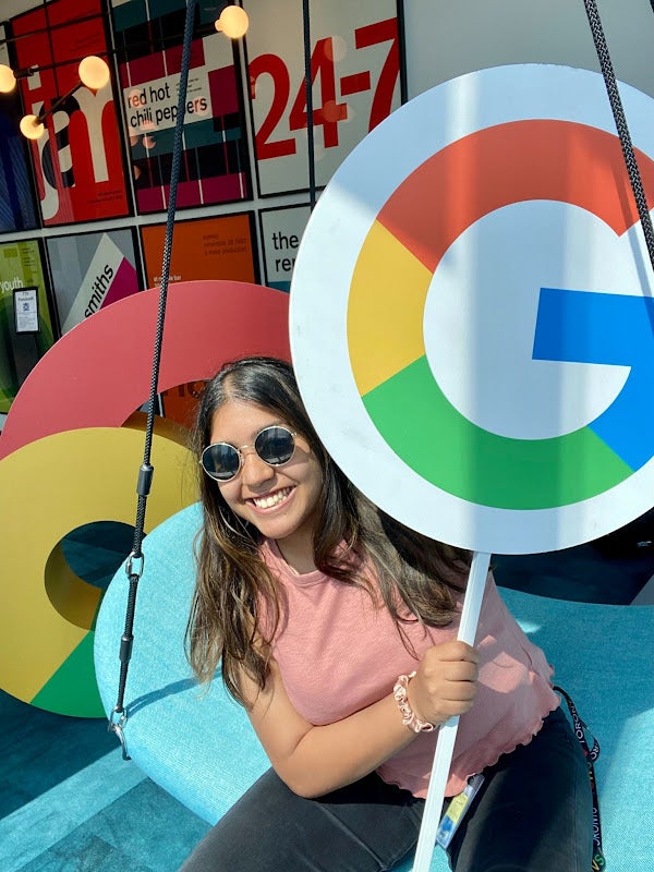 A photo of Hima smiling and holding a Google sign.