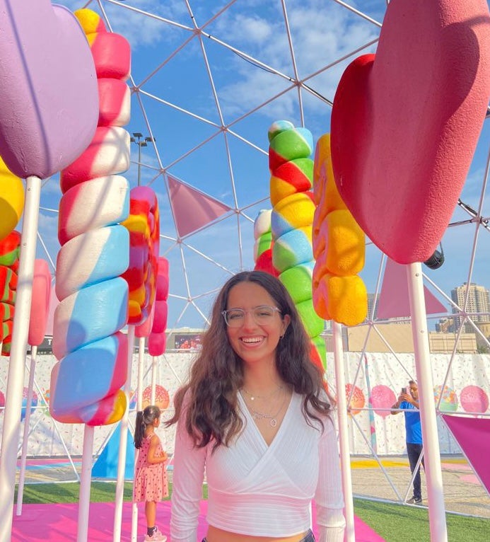 A photo of Ina standing in a cololurful art exhibit with oversized candy sculptures.
