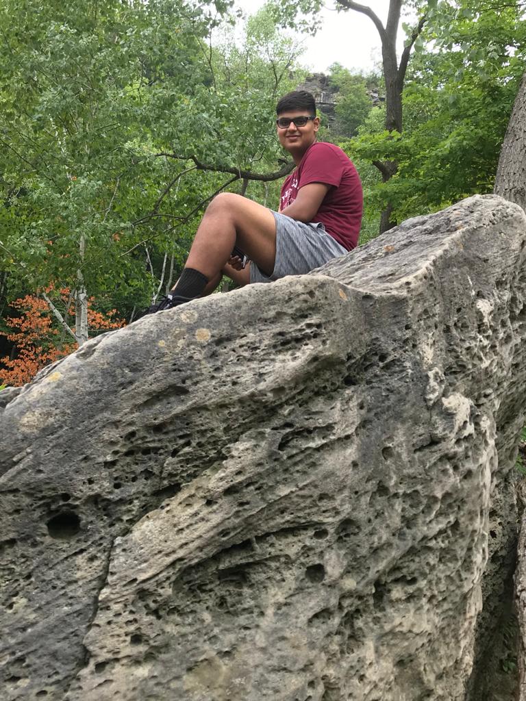 Shashwat sitting on a rock in a forest. 