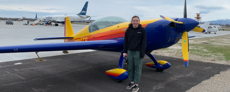 Brielle standing in front of a small, grounded, colourful plane