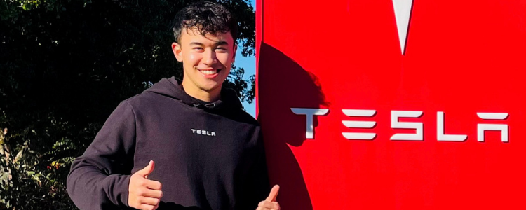 A photo of Waterloo co-op student Brandon Goh smiling and giving two thumbs up beside a Tesla sign.