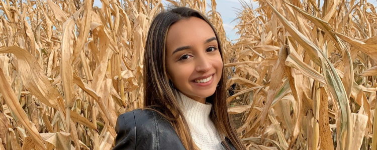 University of Waterloo Health co-op student, Sarina Nathoo, smiling outside in a corn field. 