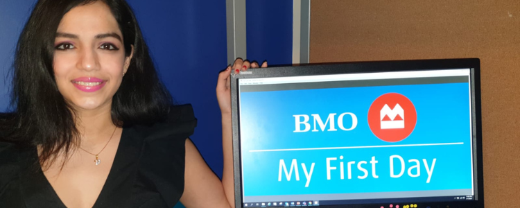 A photo of Vrushti sitting beside a computer showing an image of the BMO logo and the text, "My First Day."
