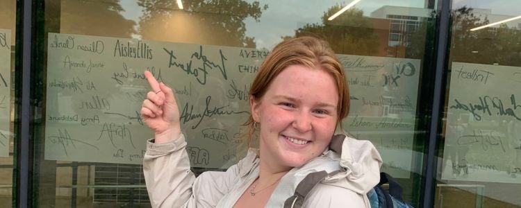 Aisley Ellis pointing to her written name on the window of Student Life Centre.