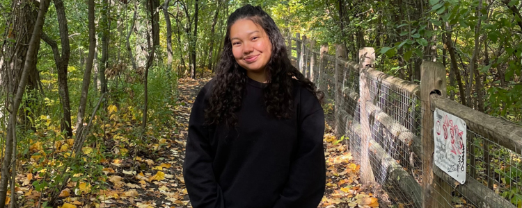 University of Waterloo student, Putri Cullinane, smiling on a trail in the woods. 