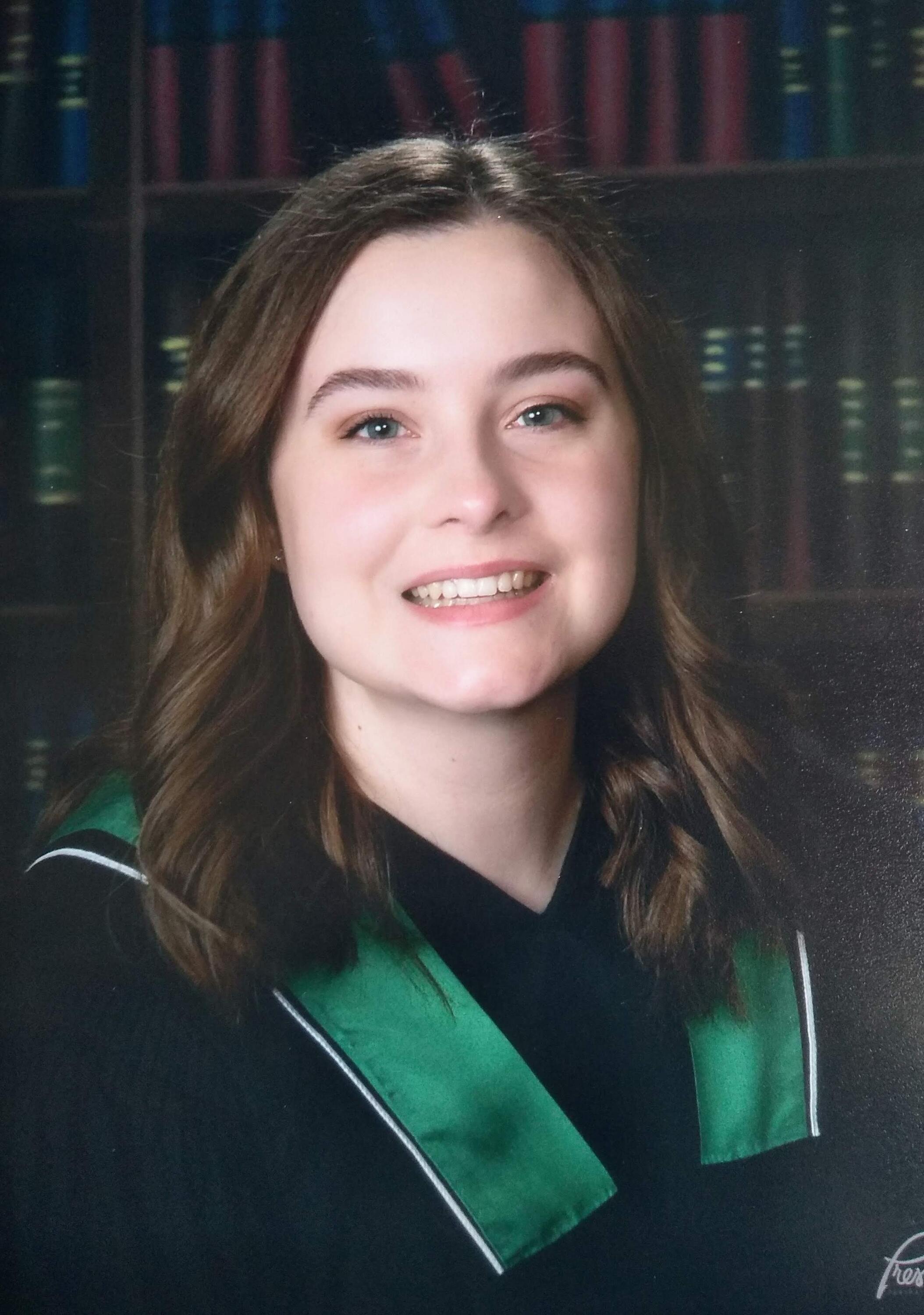 Photo of Daynica smiling, wearing a green and black graduation gown