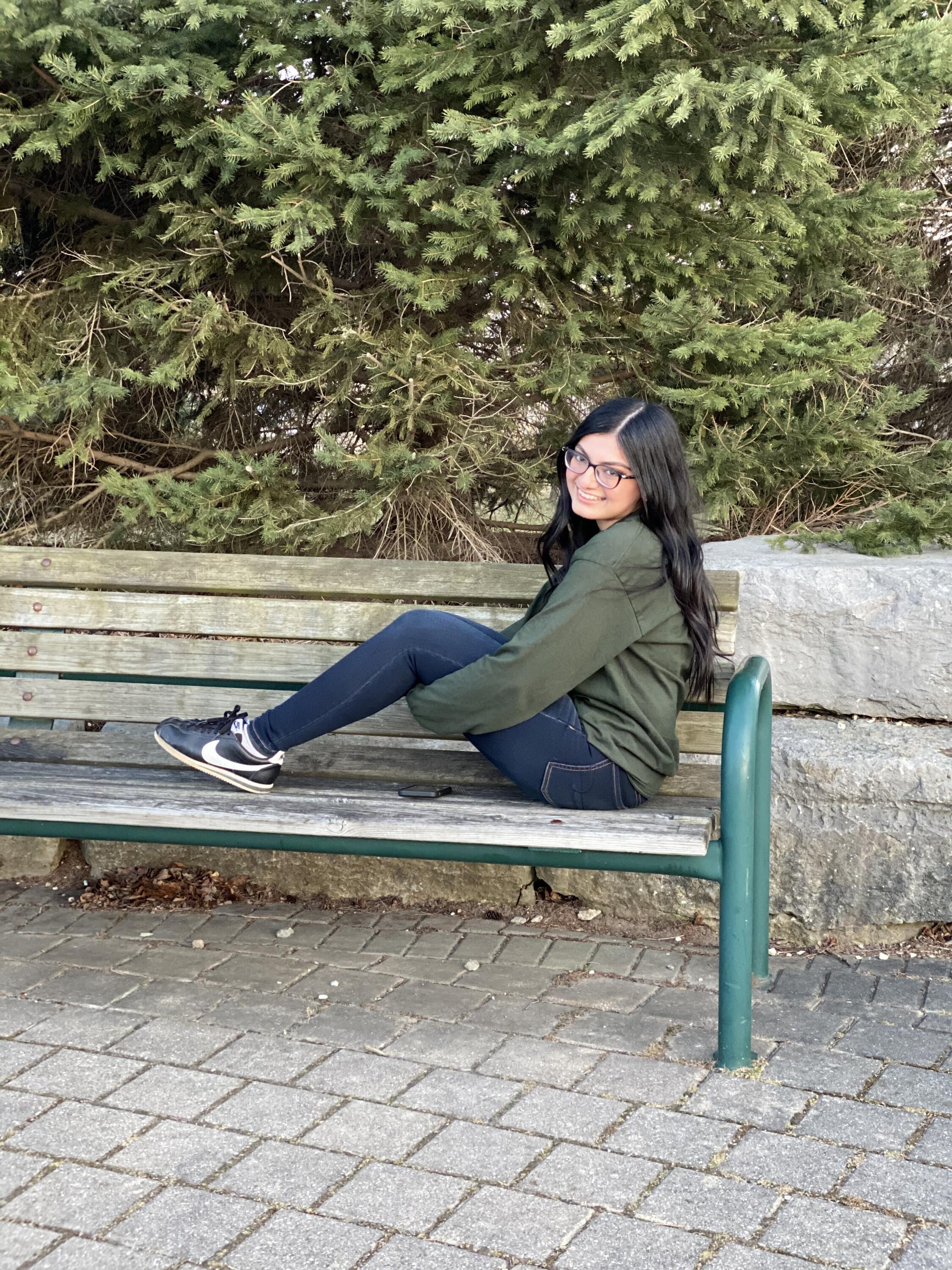 A photo of Sana sitting on a park bench outside and smiling.