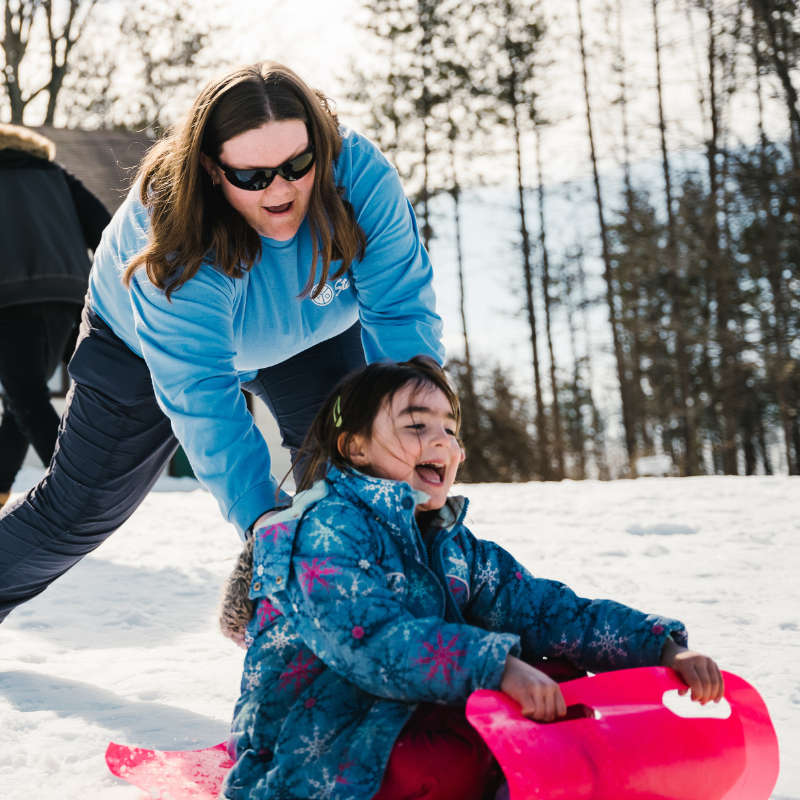 Sarah Alexander pushing a child down a hill for tobogganing