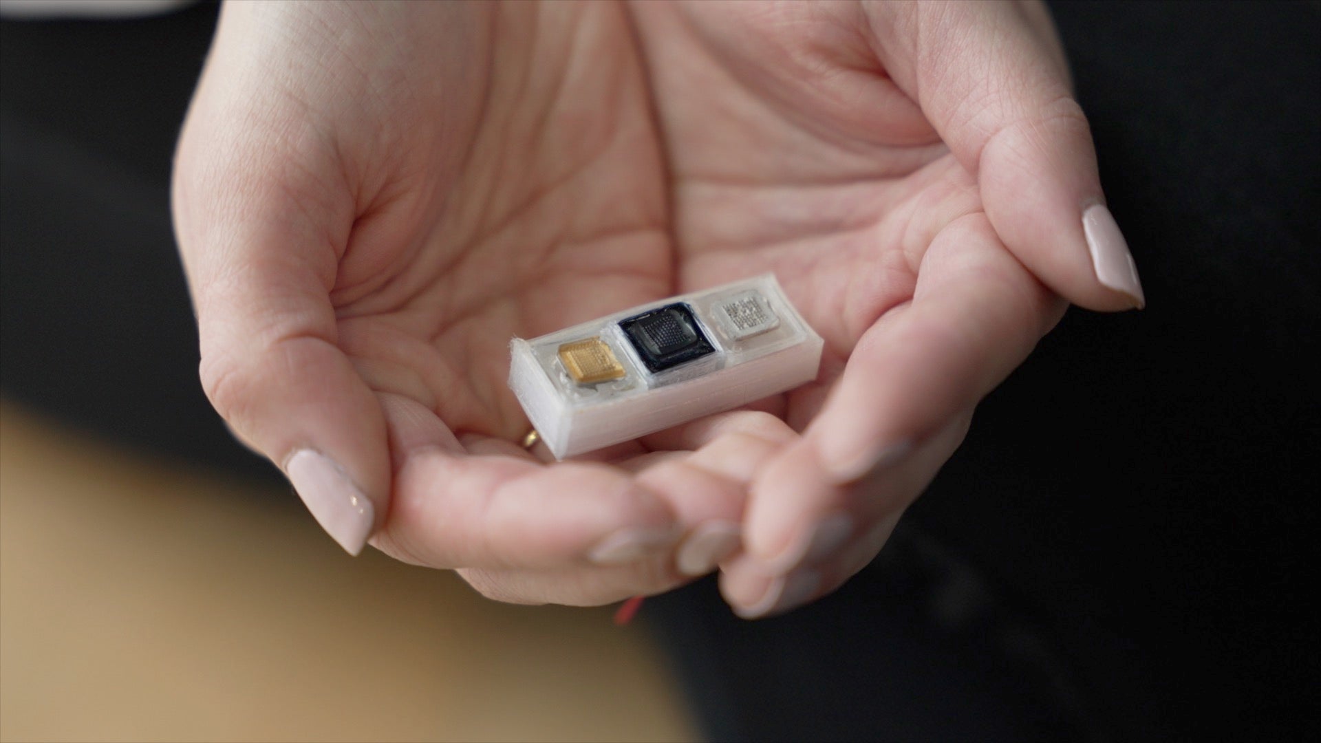 A photo of the biosensor device prototype being held in two hands.