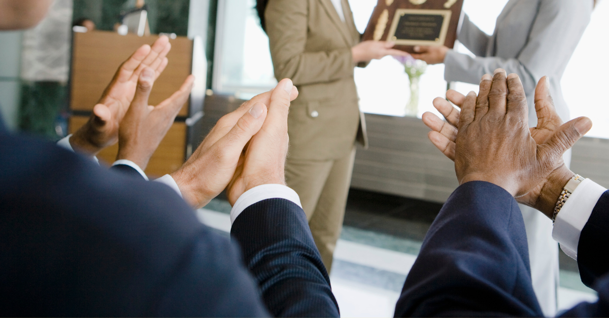 Diverse hands clapping for someone receiving an award plaque