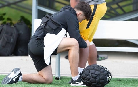 Daniel Proietti helping athlete on the sidelines of a football field
