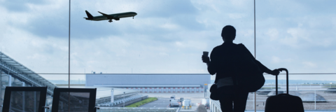 Person holding a coffee watching a plane take off at an aiport