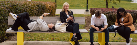 Students sitting on bench scrolling on their phones. 