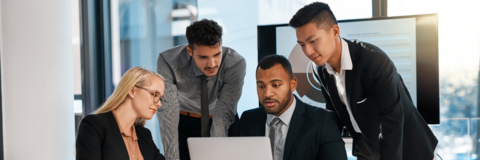 Three co-op students and advisor looking at laptop together in an office settings