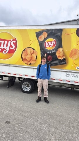 Adam Kafi stands smiling in front of a Lay's delivery truck featuring large images of potato chips and Lay's branding during his co-op work term.
