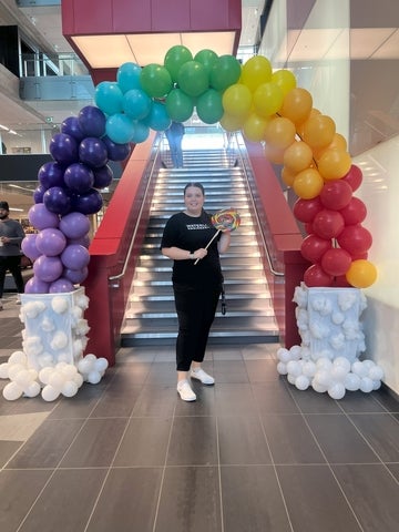 Brooke Driscoll posing in front of a rainbow balloon arch in the Engineering 7 building