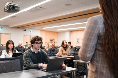 students sitting in a room with their laptops listening to woman speak