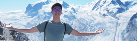 Student standing with arms open. A mountain range is behind them