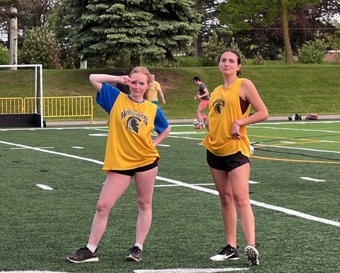 Tara Linehan and a teammate standing on a sports field in yellow intramural jerseys after a game