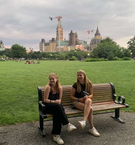 Tara Linehan and a friend sitting on a bench in front of Parliament Hill in Ottawa