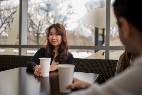 student sitting at a table with a cup in hand looking at camera