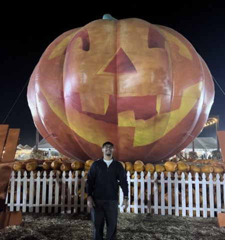 Dev Shah smiling in front of an inflatable jack-o-lantern