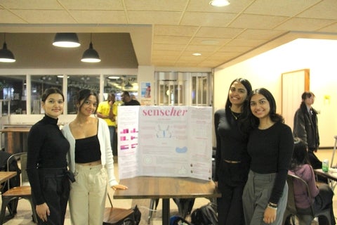 Disha Patel smiling with a group and a poster board at the Velocity Innovation Challenge