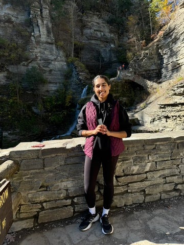 Harleen smiling/posing in front of a stone wall and mountain