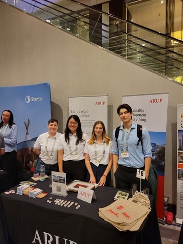 Ethan stands with fellow Arup representatives behind a recruitment booth at a career fair.