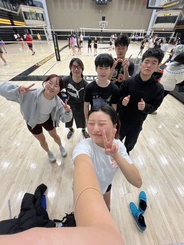 Hannah and a group of students posing for a selfie on an indoor volleyball court during a recreational sports game.