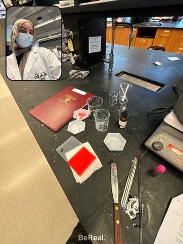 Ayesha works in a laboratory, with glassware and testing materials arranged on a lab bench in front of her.