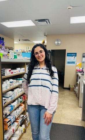 Mera stands smiling in the aisle of a pharmacy during her co-op work term.