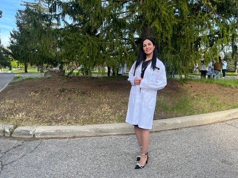 Mera Yousef smiling/posing in front trees wearing a lab coat