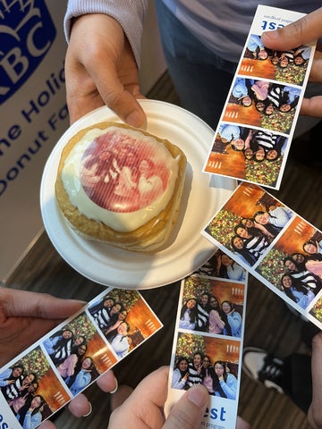 Several people hold photo booth strips around a latte with heart-shaped latte art on a table.