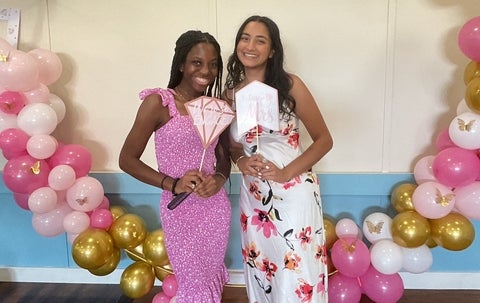 Kelly Ramnarais posing with a friend in front of a pink balloon garland 