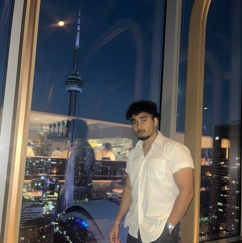 Rafin Khan posing in front of a window with the CN tower in the background