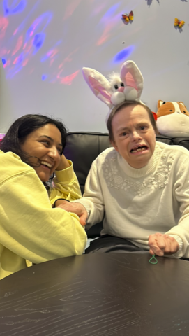 Kelly Ramnarais sitting on a sofa with a lady who's wearing bunny ears