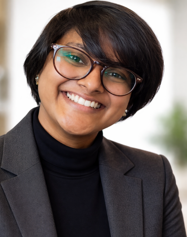 Vanya Gnaniah headshot, smiling at the camera wearing a grey blazer and black shirt