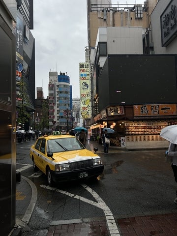 A yellow taxi driving along a busy street surrounded by buildings and storefronts in Japan.