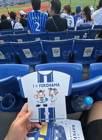 A hand holding a Yokohama football match program while seated in a stadium overlooking the field.