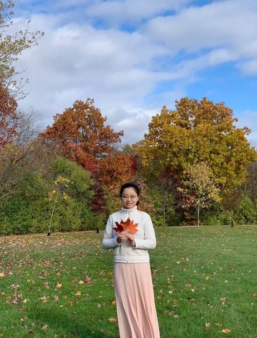 Yunxing Zhang holding autumn leaves outdoors during the fall season