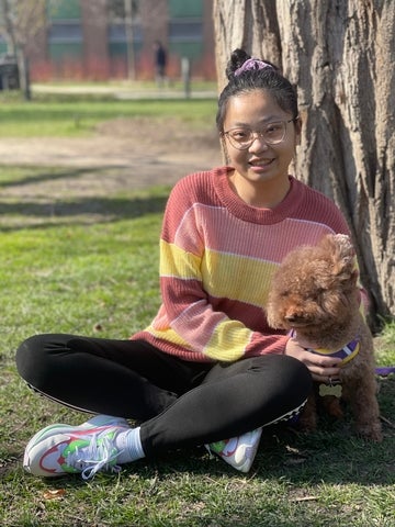 Yunxing Zhang sitting outdoors with a dog during a sunny day in the park