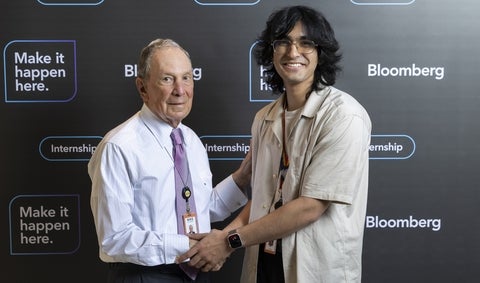 Zain smiling and shaking hands with colleague in front of a Bloomberg backdrop