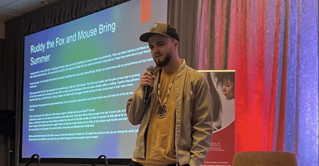 Indigenous student, Ethan Gardner with a mic standing in front of screen showing he slides as he gives a presentaion